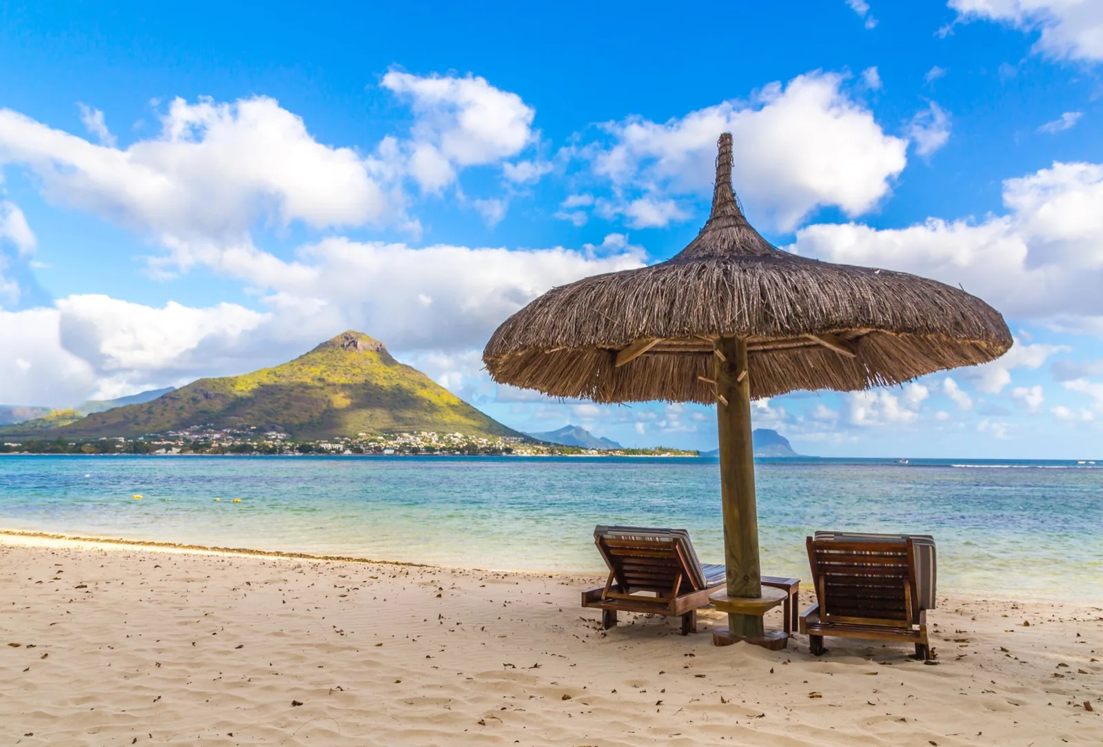 White-sand beach with a thatched sun shade and mountain views on the west coast of Mauritius
